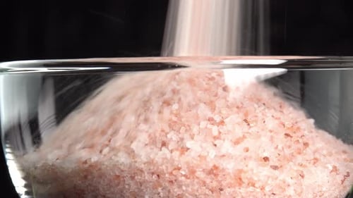 Pink himalayan salt or rock salt pouring in glass bowl. Trace minerals salt used for cooking