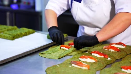 Unusual green crepes are rolled with cheese and salmon fish. The cook rolls the pancakes