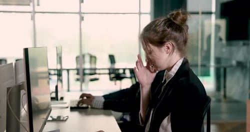 Businesswoman working at desktop computer in modern office alongside male colleague. Focused startup