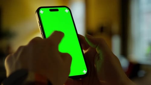 Person Holding Smartphone with Bright Green Chroma Screen and Cross Markers in Cozy Indoor Setting
