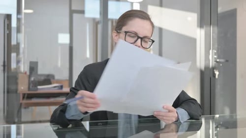 Woman Reads Papers and Writes at Office Desk