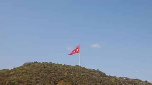 Red Flag Waving on Hill Under Blue Sky