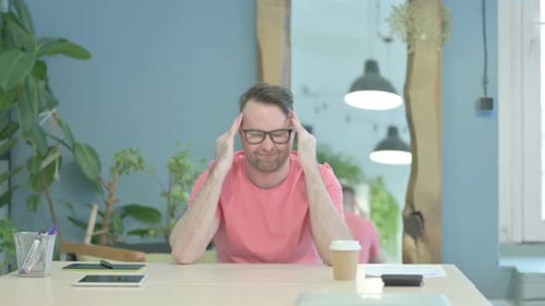 Man Rubbing Head at Desk Indoors