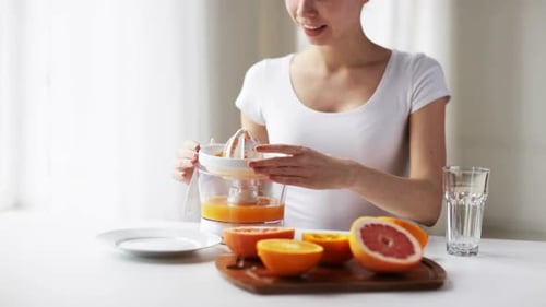 Jeune femme souriante pressant du jus d'orange et de pamplemousse frais à la maison pour une alimentation saine