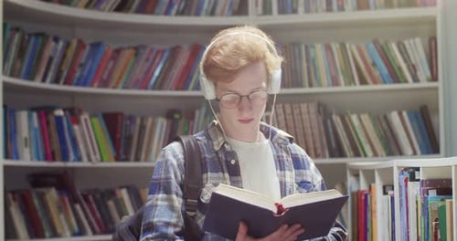 Young Man Reading Book in Library with Headphones
