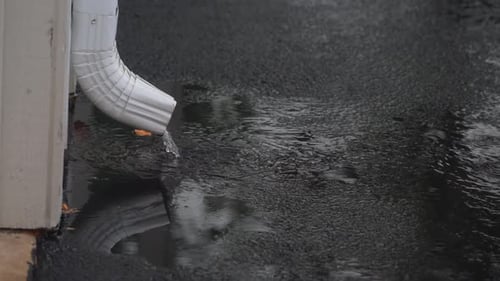 Rainwater Flowing from White Downspout Creates Puddles