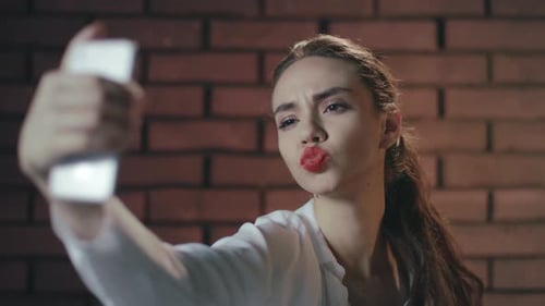 Attractive young woman takes selfie in front of brick wall
