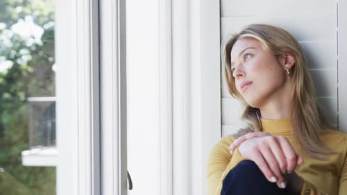 Thoughtful biracial woman looking through window at home, slow motion, copy space