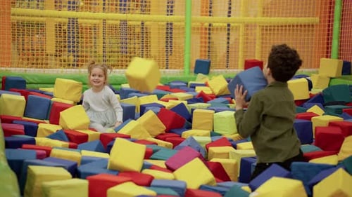Jolie petite fille et garçon jouant avec des cubes mous dans la piscine sèche du Game Center et s'amusant lentement