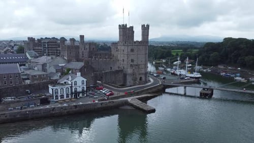 Ancient Caernarfon castle Welsh harbour town aerial view medieval waterfront landmark slow descend