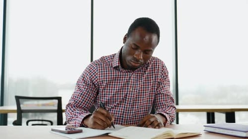 African American Student Sits in Library Prepare for Exam and Making Notes in Notebook