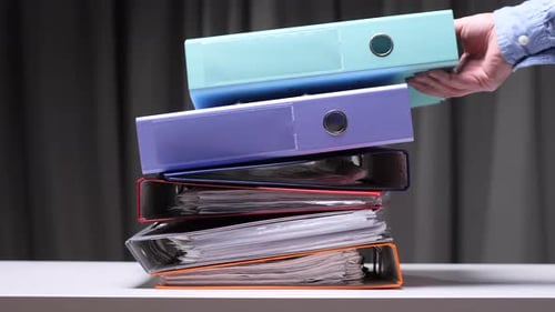 Mann nimmt einen Ordner aus einem Stapel bunter Ringbücher auf dem Schreibtisch
