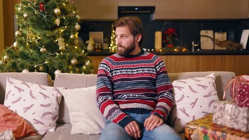 Portrait of Tired Caucasian Bearded Man Sitting Near Christmas Tree Hesitating Spending Holidays