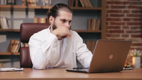 Serious Man with Tiedback Hair Working on Laptop in Office