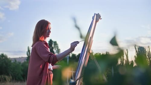 Woman Painting Outdoors in Rural Setting at Sunset