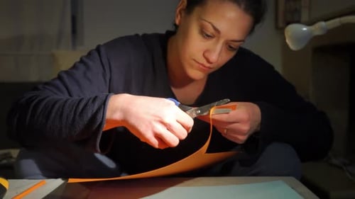 Woman Cuts Orange Paper with Scissors at Night