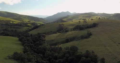 A backlit, 4k wide aerial tracking drone shot over lush green hills on a clear day.