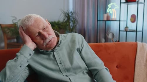Mature Man Massaging Temples on Orange Couch