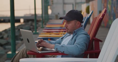 Man Works on a Laptop While Sitting on a Bench Outdoors