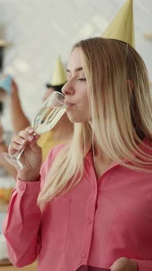 Woman Drinks Champagne and Looks at Phone at Party