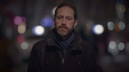 Man With Glasses Stands on City Street at Night