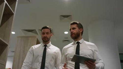 Business team managers talking corporate data using tablet walking in office hallway