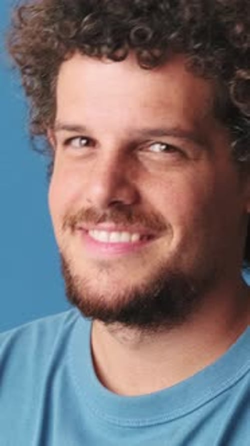 Close up, young man looking at camera and smiles isolated on blue background in studio