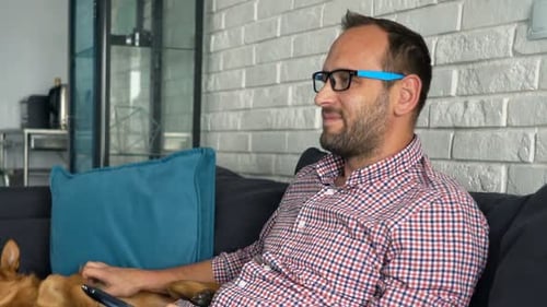 Man relaxes on couch petting dog watching television