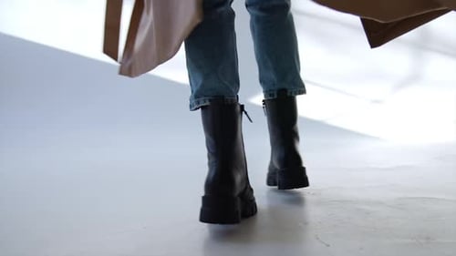 Massive black army boots with laces on a model wearing jeans and beige coat.