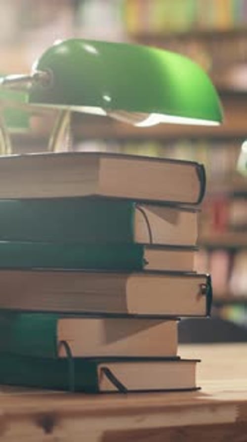 Vertical Video Stack of Books Placed on Empty Library Table with Green Lamps Near Bookshelves