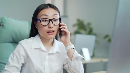 portrait a young asian business woman worker talking on mobile phone in office sitting at desk