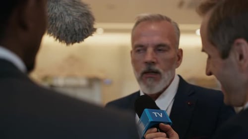 Man Gives Interview Surrounded by Microphones Indoors