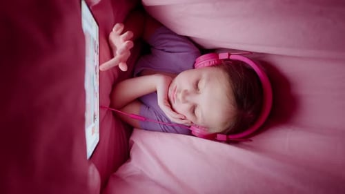 Child Using Tablet With Headphones Under Blanket