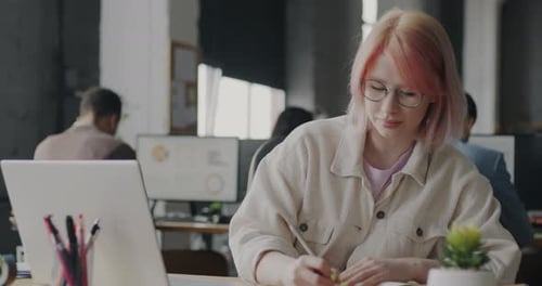 Young Lady Working with Laptop and Writing Information in Notebook in Coworking Place