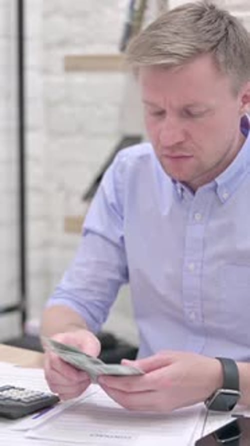 Man Counting Money and Using Calculator Indoors