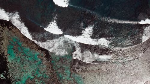 Aerial view of coastline with crashing waves and vibrant coral reefs