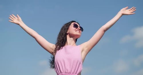 Woman Smiling, Arms Raised Against Blue Sky