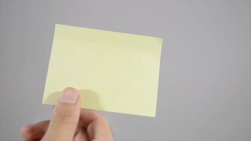 Hand Applying Yellow Sticky Note to Gray Surface