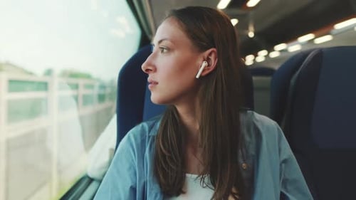 Young woman in wireless earphone into ear traveling by suburban train
