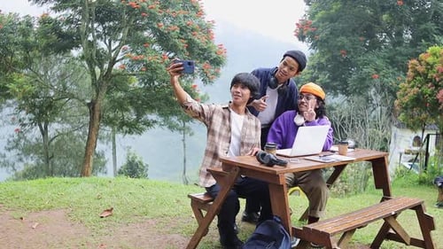 Friends happily taking selfie together while working remotely outdoors on laptop