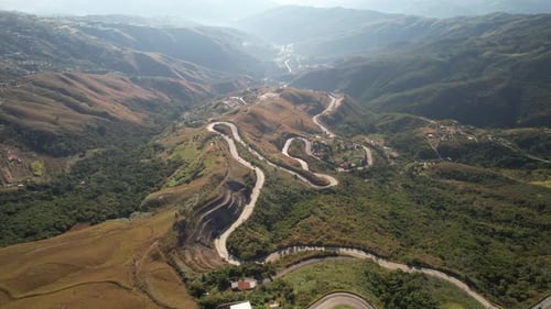 Aerial view of winding mountain road curving through lush green hills and valleys