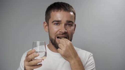 Man Takes Vitamin Capsule with Water Close Up