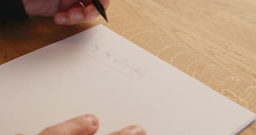 Nahaufnahme des Schreibens eines Testamentsentwurfs. Mann schreibt mit linker Hand auf ein Blatt Papier und legt