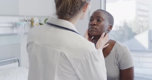 Diverse female patient and doctor checking her neck with hands in hospital, in slow motion