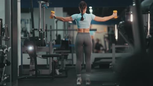Fit Woman Exercising Deltoids with Dumbbells in a Gym