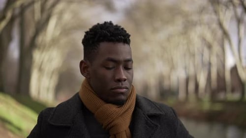 Contemplative man walking outside at park during winter wearing coat and scarf