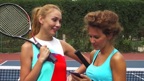 Young Adults With Tennis Rackets Looking At Phone