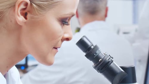 Woman Looks Through Microscope in Bright Modern Laboratory