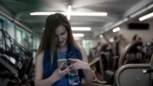 Young woman in gym takes selfie with smartphone after workout