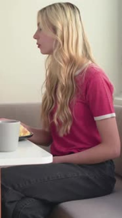 Vertical video: Hearing offscreen voice, lady in red top turning head at home, lifting gray mug